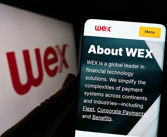 A smartphone screen displays a website with the heading "About WEX." It describes WEX as a global leader in fintech solutions, simplifying payment systems for industries like fleet, corporate payments, and benefits. In the background, the WEX logo is prominently visible.