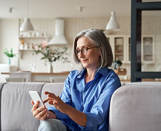 An older woman using a smartphone at home, representing VividCloud's development of a secure, HIPAA-compliant telehealth platform on AWS.