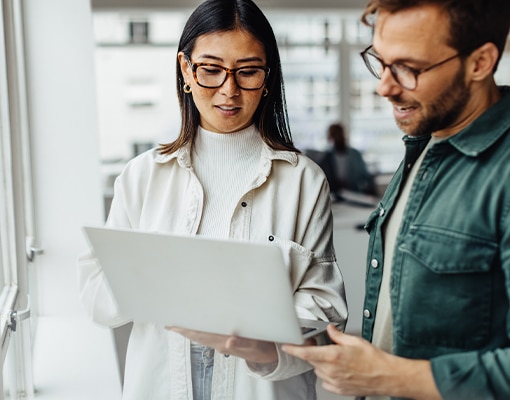 a man looking at a laptop with a woman in a modern office