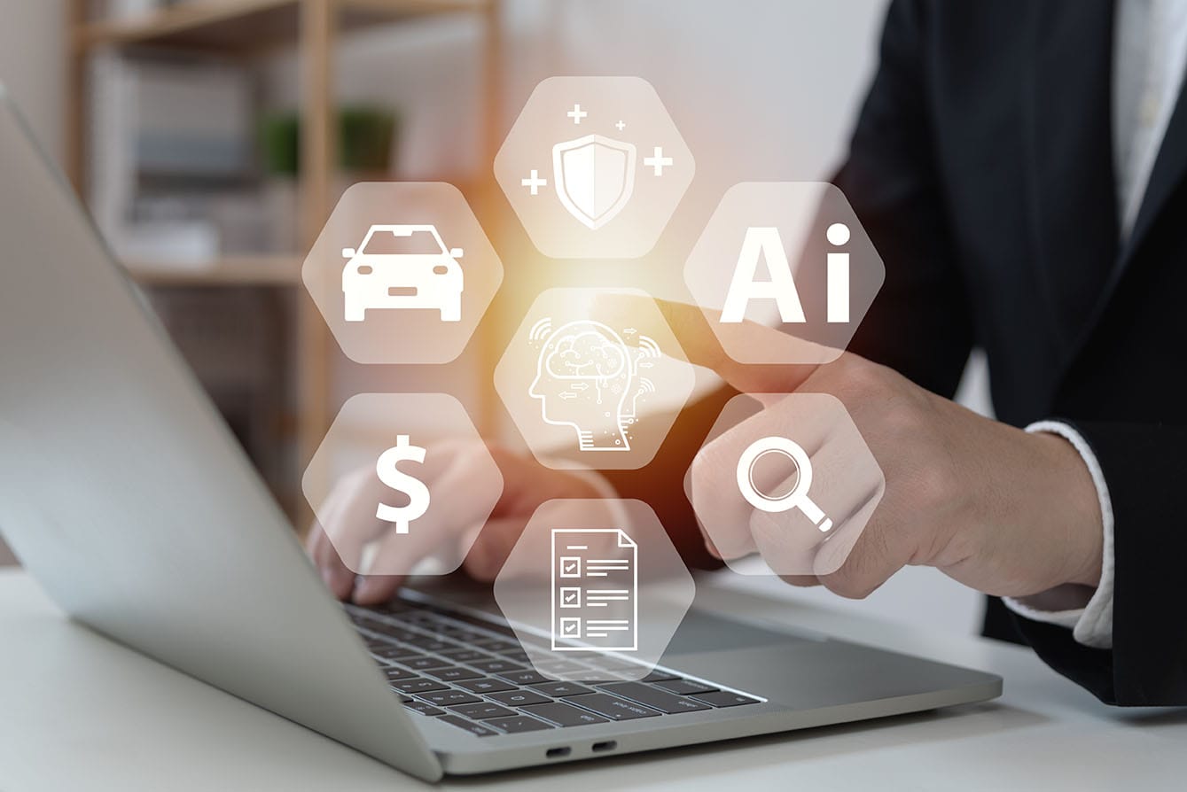 A person in a suit is using a laptop. Various icons are overlaid around the user’s hands, including a car, dollar sign, document, magnifying glass, shield, and an AI head. These icons suggest concepts related to technology, AI, insurance, and finance.